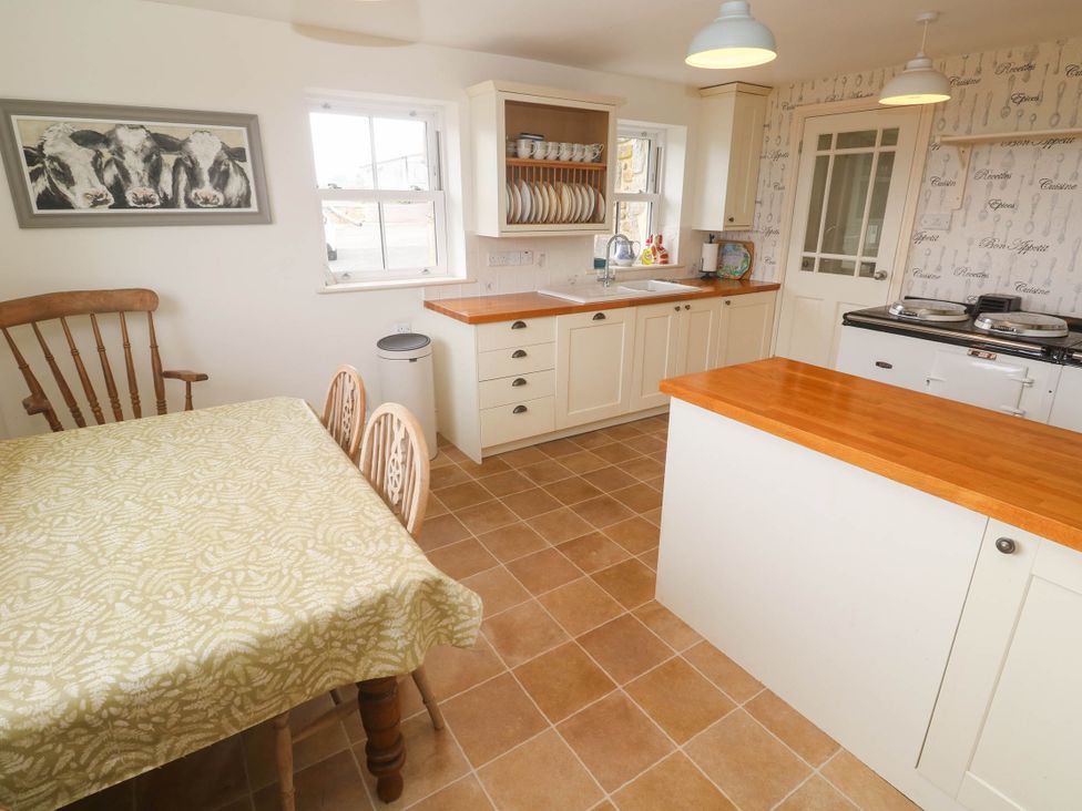 A kitchen with a dining table and chairs, sink, cabinets, and oven at Chyrose Farmhouse in Pendeen
