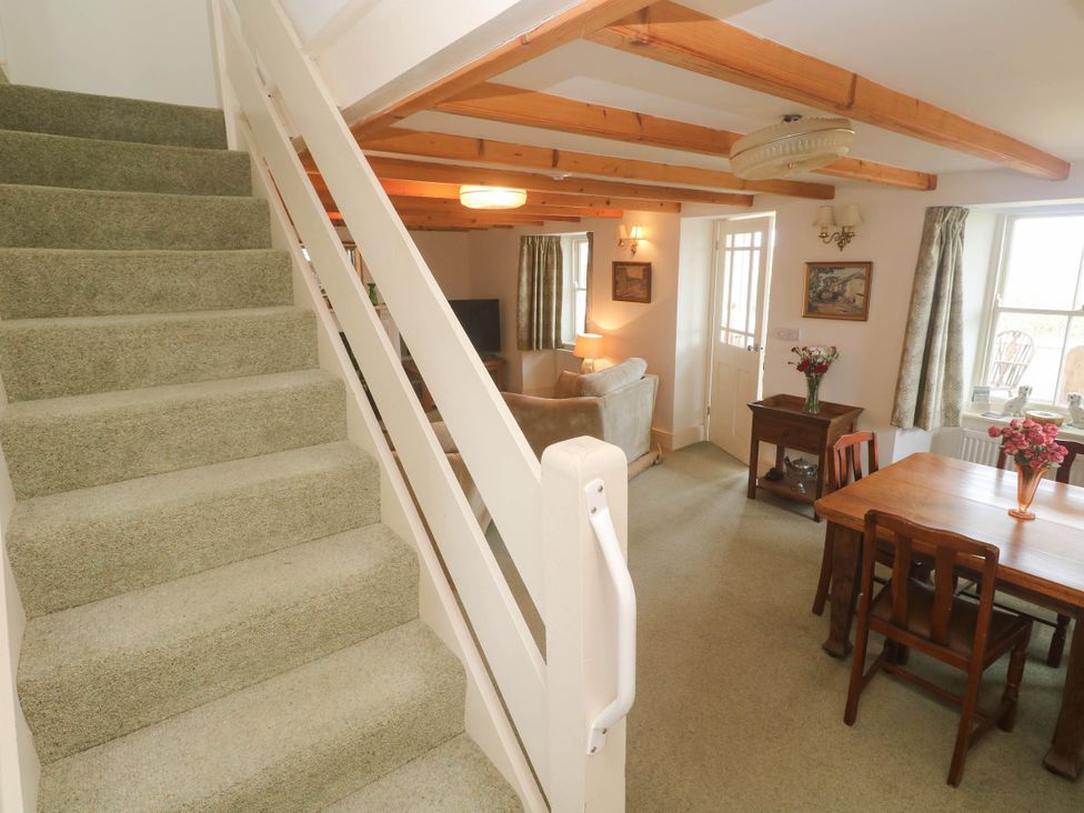 A living room with a staircase and dining area at Chyrose Farmhouse in Pendeen