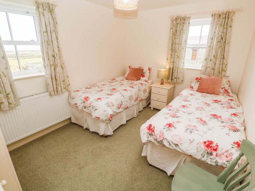 A bedroom with two beds and a bedside lamp at Chyrose Farmhouse in Pendeen