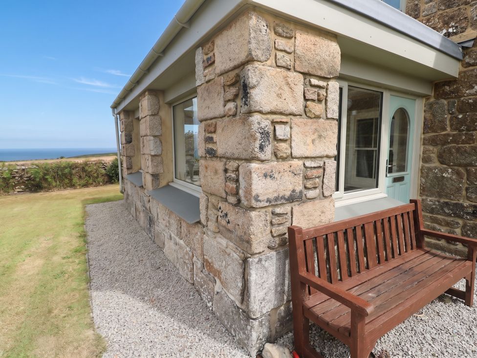 An outdoor area with a stone wall and a wooden bench at Chyrose Farmhouse in Pendeen