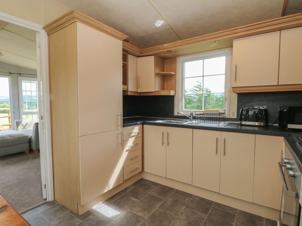 A kitchen with cabinets, sink, and window at Hawks View Caravan in Macclesfield