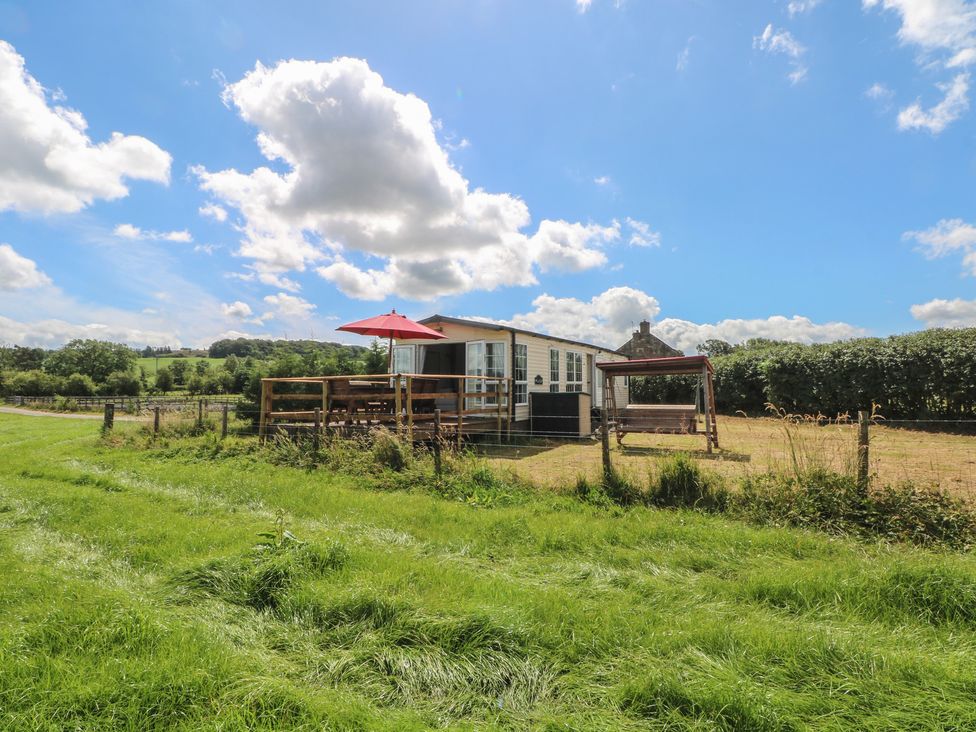 A caravan with a deck and umbrella at Hawks View Caravan in Leek