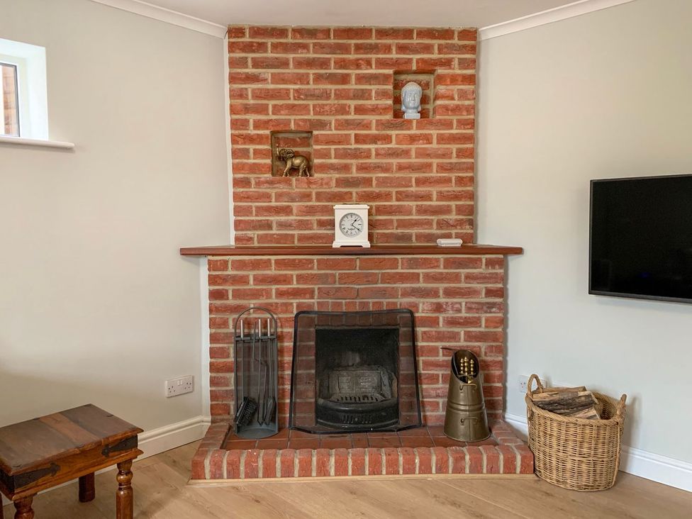 A living room with a fireplace and wall-mounted TV at The Cottage in Winterslow