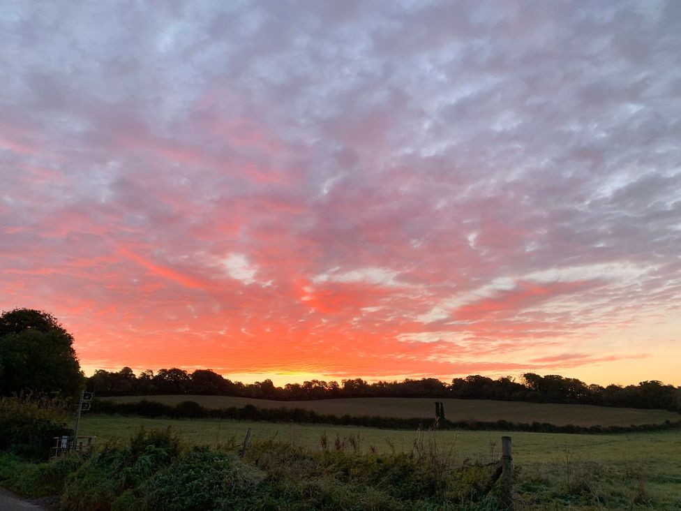 A sunset with colorful clouds and trees in the background at The Cottage in Winterslow