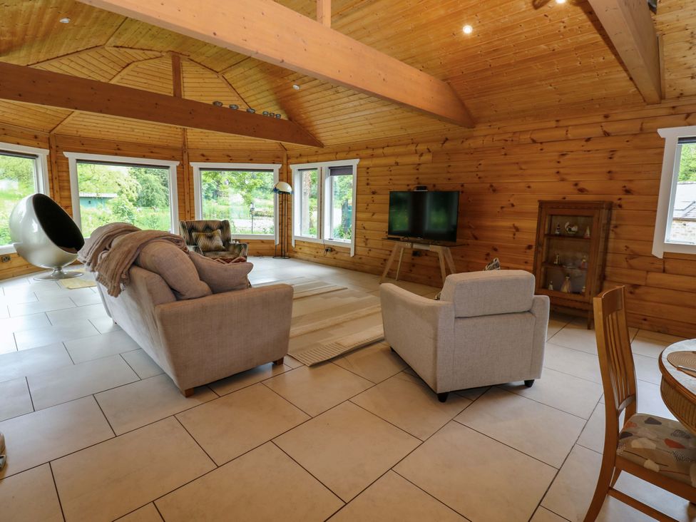 A living room with a sofa, armchair, and television at Bull Rush Cabin Carwinley near Longtown