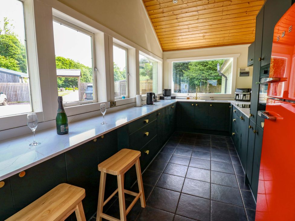 A kitchen with bar stools and windows at Bull Rush Cabin in Carwinley near Longtown