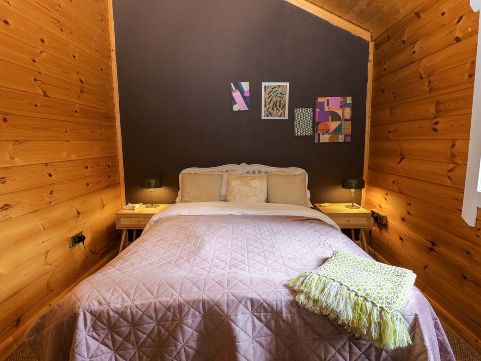 A bedroom with a bed, bedside tables, and wall art at Bull Rush Cabin in Carwinley near Longtown