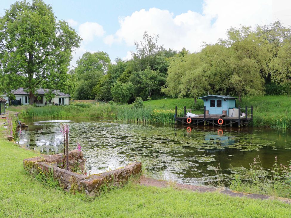 A pond with a dock and small cabin at Bull Rush Cabin Carwinley near Longtown