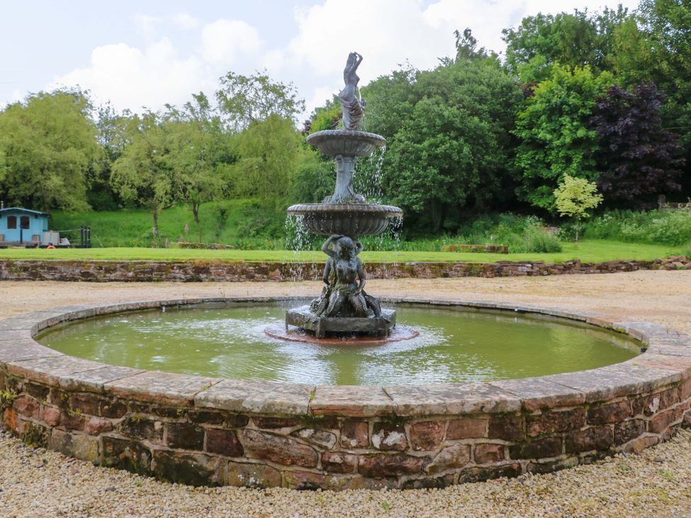 A fountain surrounded by gravel and trees at Bull Rush Cabin in Carwinley near Longtown