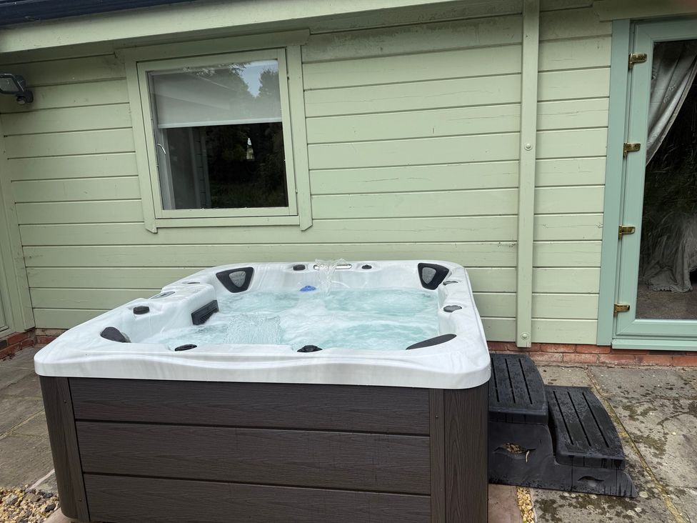 A hot tub next to a green exterior wall and window at Bulrush Cabin Carwinley near Longtown