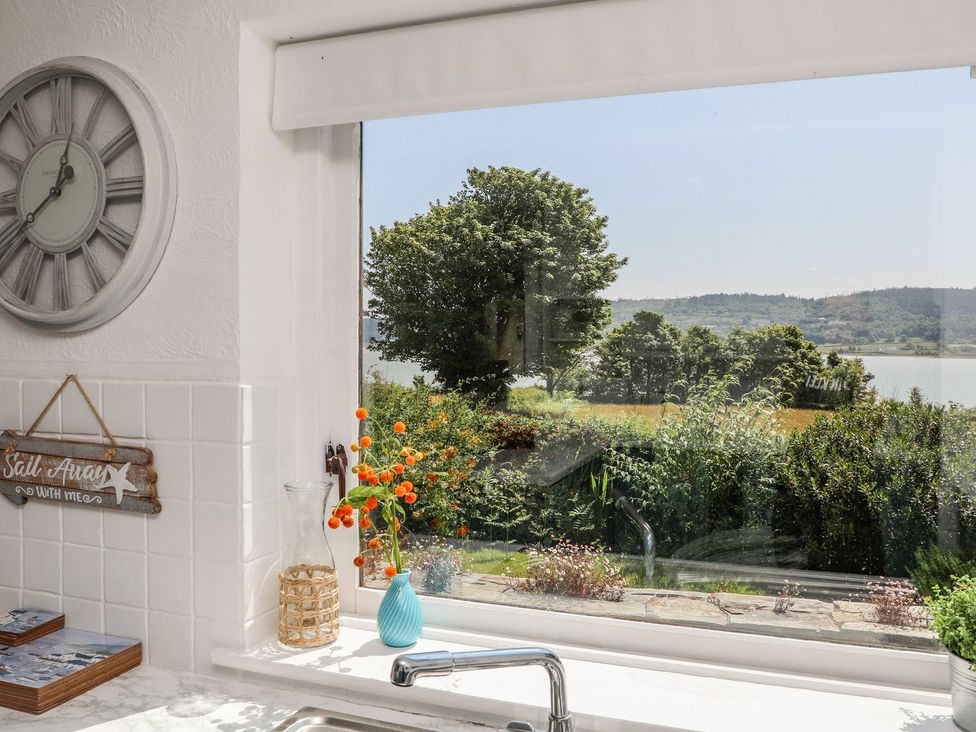 A kitchen with a view of a garden and water at Bryn Llifon in Pentraeth