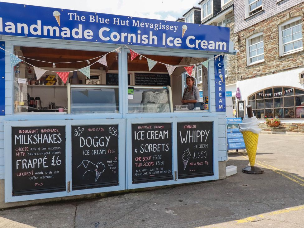 An ice cream stall with menu boards and an employee at The Blue Hut in Mevagissey