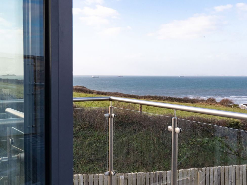 A balcony view of the ocean with a glass railing at One Sand Banks Haverfordwest
