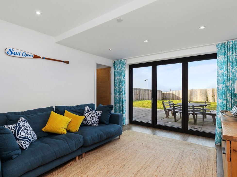 A living room with a sofa and sliding doors leading to an outdoor patio at One Sand Banks in Haverfordwest