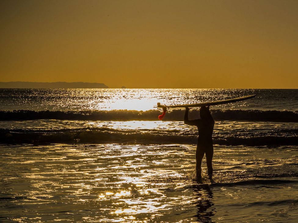 A surfer carrying a surfboard walking through the ocean at sunset