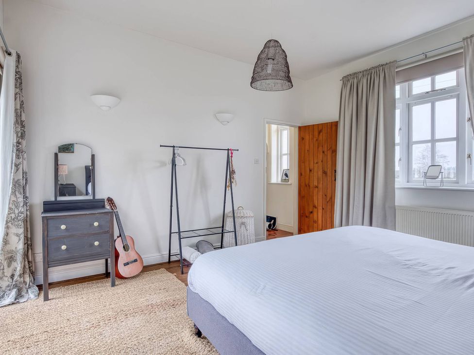 A bedroom with a bed, dresser, clothes rack and guitar at TBC