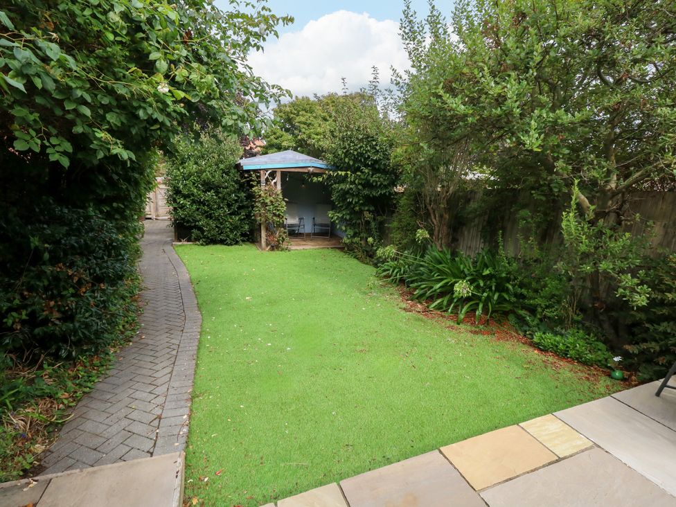 A garden with grass and a pathway leading to a patio at 29 Bincleaves Road Weymouth