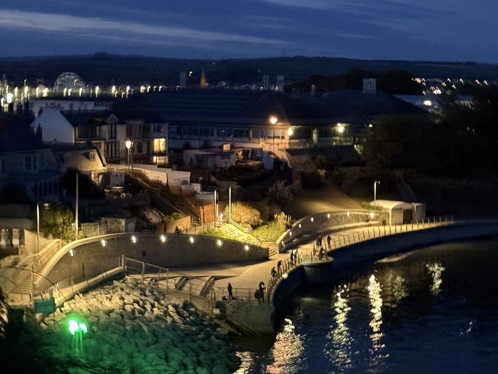 A nighttime waterfront view with a walkway and buildings at Coast Path Cottage in Weymouth