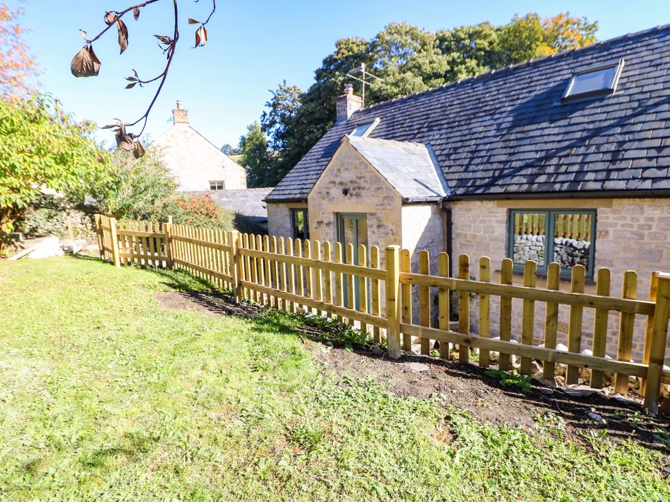 A garden area with a wooden fence and a stone cottage exterior at Stone Lily Cottage