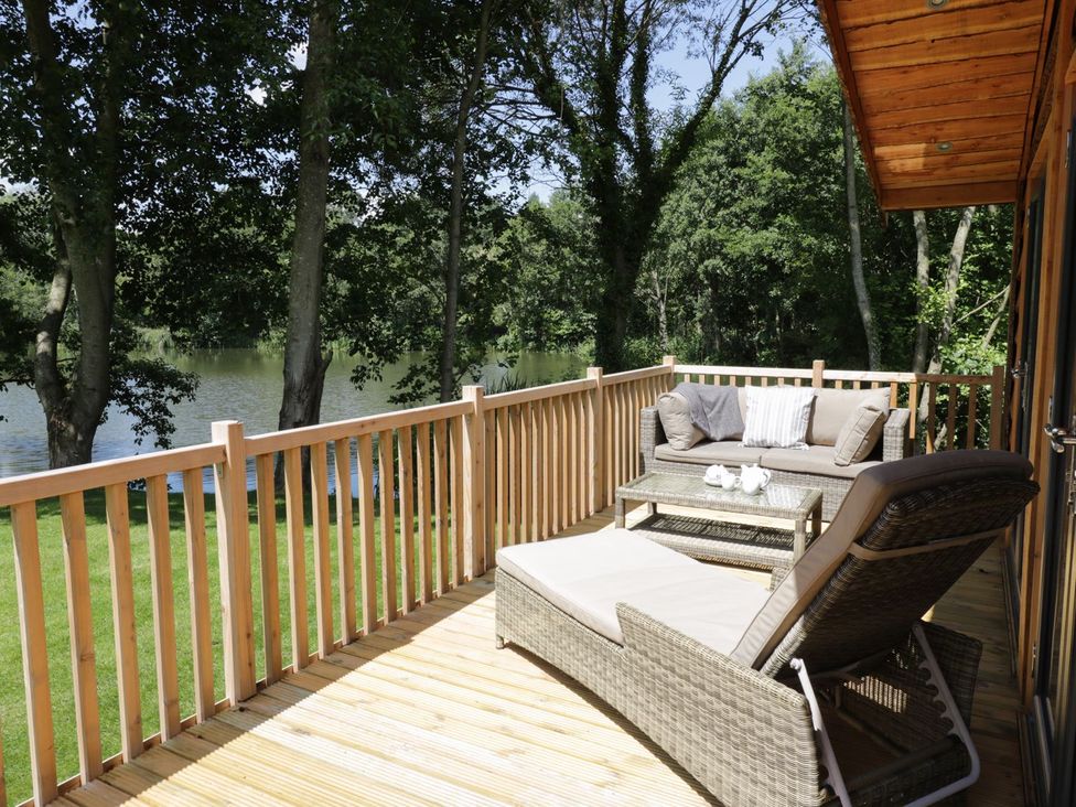A deck with outdoor furniture overlooking a lake at Kingfisher in Ross-on-Wye