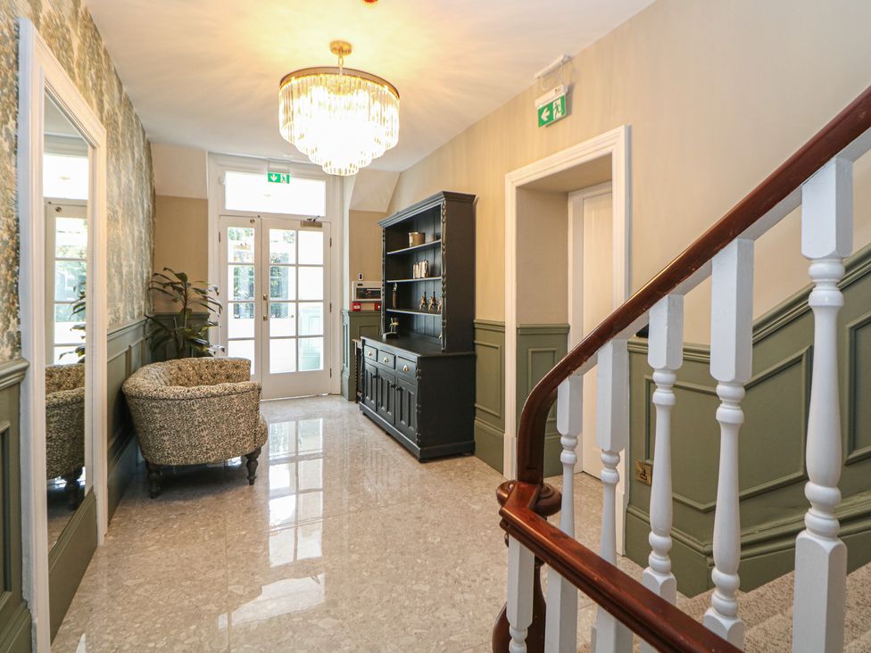A hallway with a staircase and a chair at The Pavillon Suite in Buxton