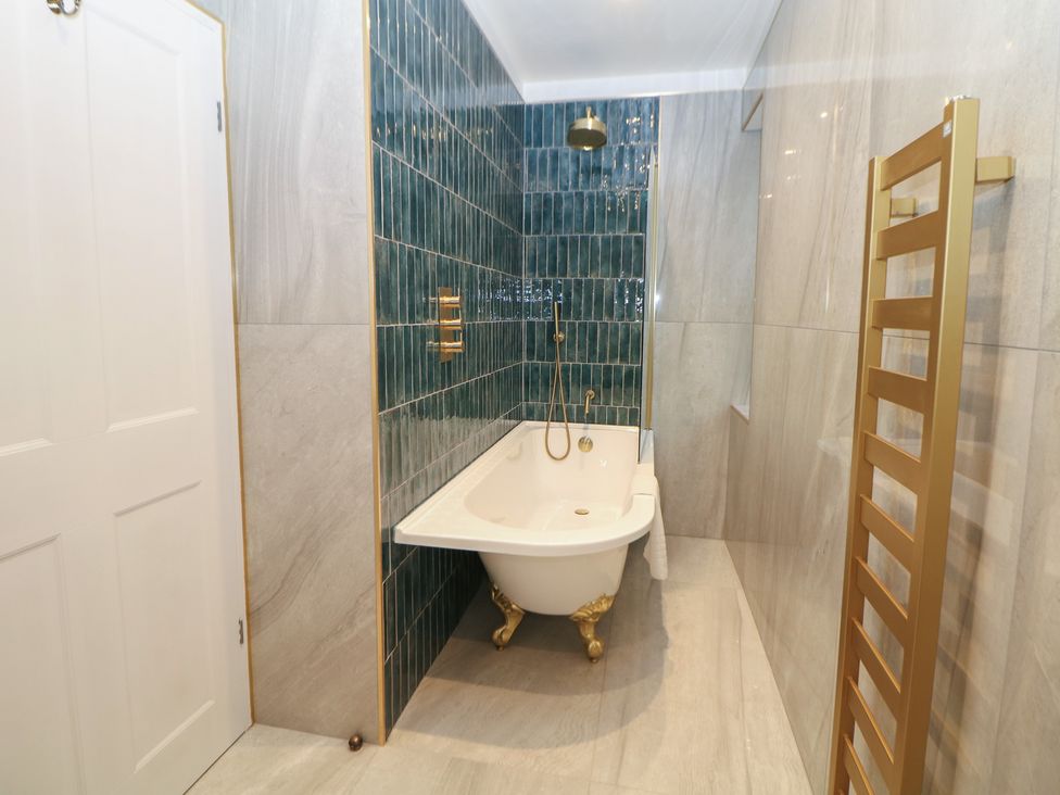 A bathroom with a bathtub and green wall tiles at The Chatsworth Suite in Buxton
