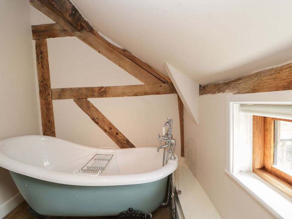 A bathroom with a bathtub and wooden beams at The Old Barn in Hereford