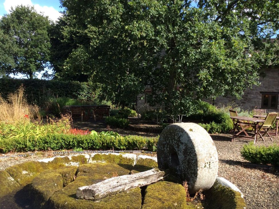 A garden with a stone wheel and wooden table at The Old Barn in Hereford