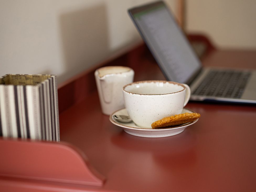 A cup and saucer with a cookie and a laptop at Ambersham House in Midhurst