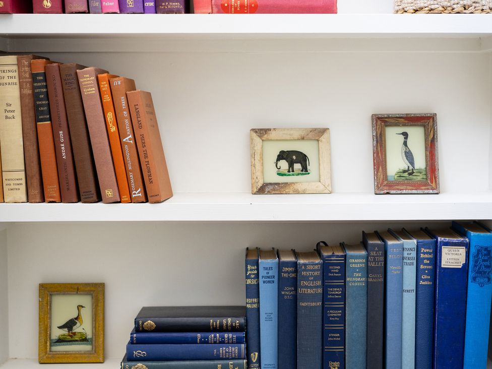 A bookshelf with books and framed pictures at Ambersham House in Midhurst