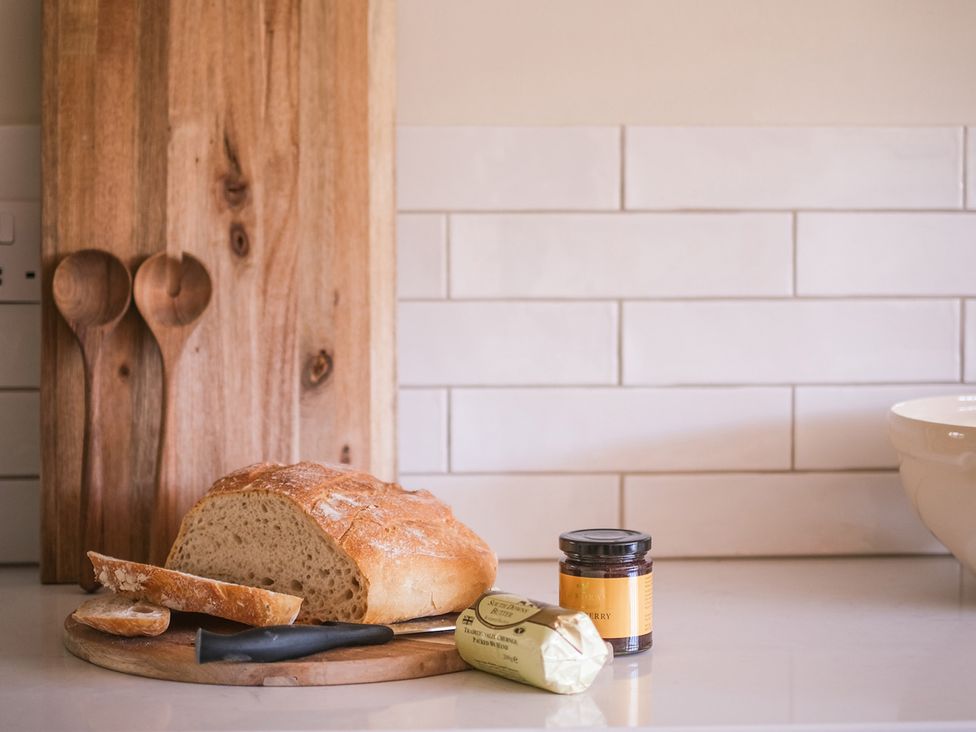 A kitchen countertop with bread, knife, cutting board, jar and butter at Challens Yarde in Midhurst