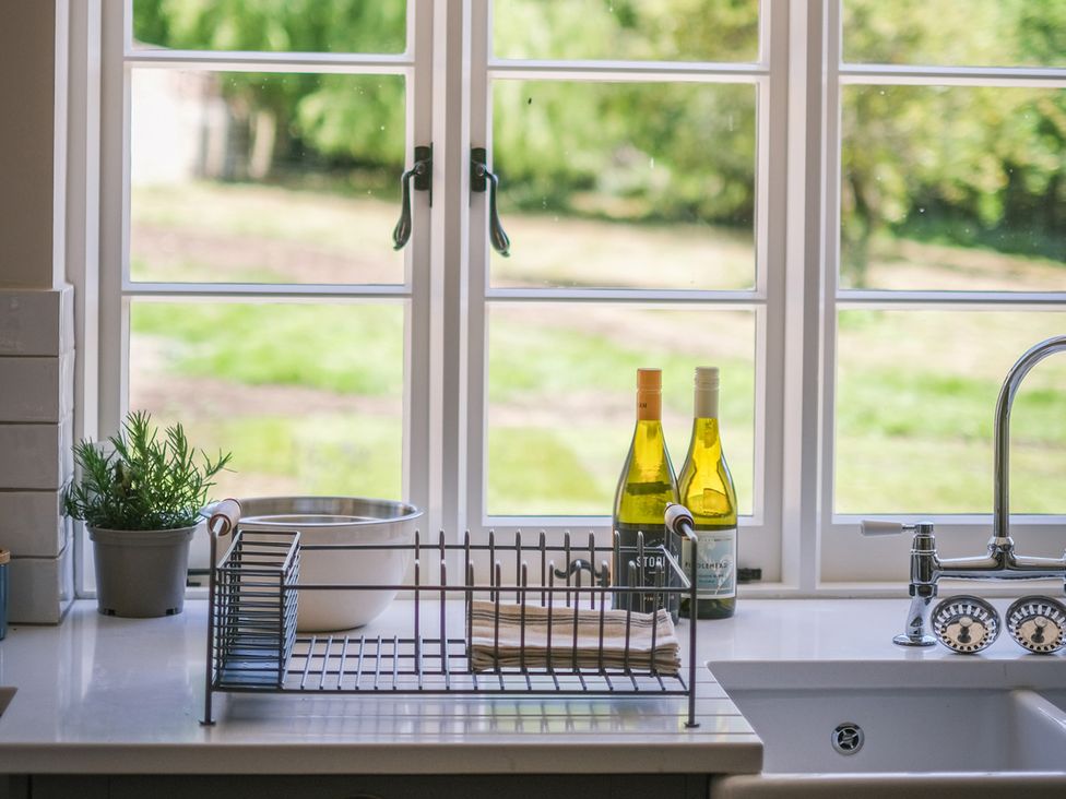 A kitchen with a sink, dish rack, bowl and wine bottles at Challens Yarde in Midhurst