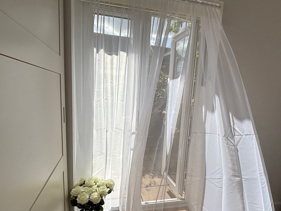 A window with curtains and flowers at Oakwood Annexe Colchester