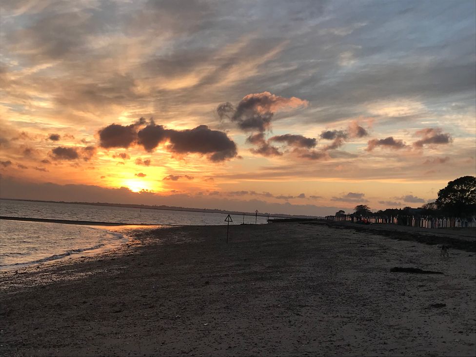 A beach at sunset with a sign and beach huts in the distance at Oakwood Annexe in Colchester