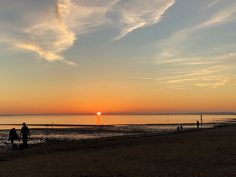 A sunset over the ocean with silhouettes of people on the beach at Oakwood Annexe in Colchester