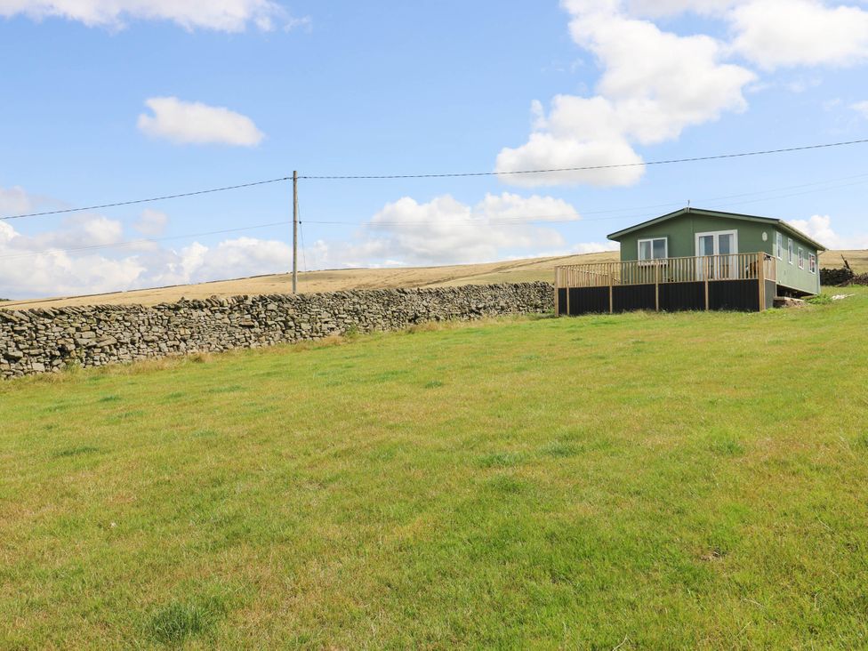 A house with a stone wall and grass area at Lodge in High Peak