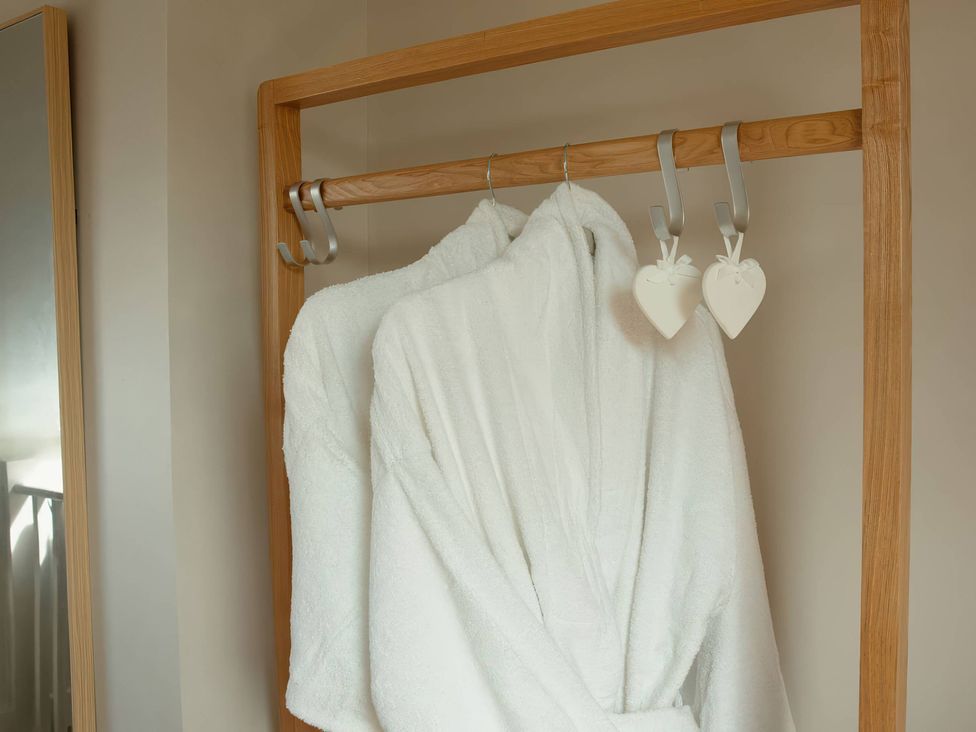 Two white bathrobes hanging on a rack with a mirror in the bathroom at TBC