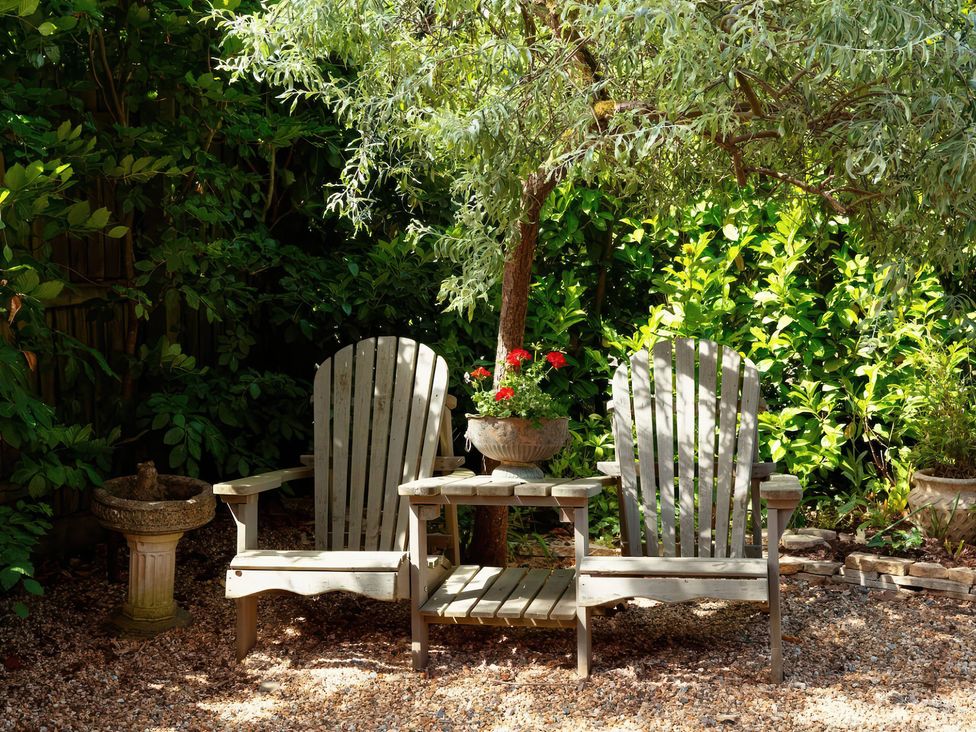 A garden with adirondack chairs and a side table under a tree at TBC