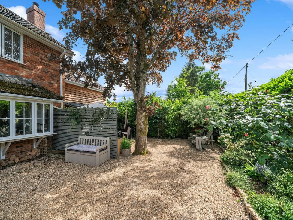 A garden area with gravel, a tree, benches, and shrubs at TBC