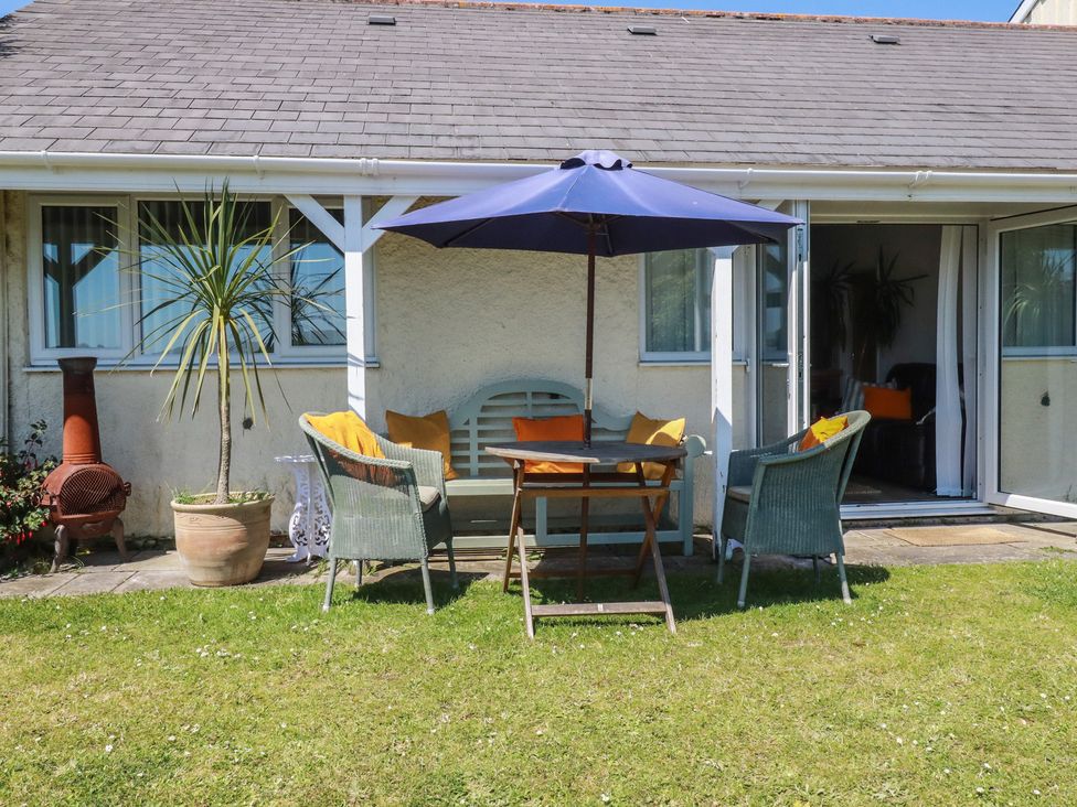 A patio area with a table and chairs under an umbrella at Rollies Retreat in Fowey