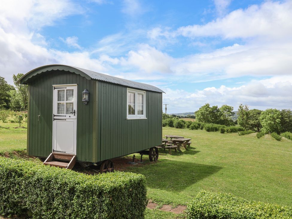 A shepherd's hut with a door and windows on a grassy area at Shepherds Hut at East Hill Pride Four Elms Hill Nr. Sidmouth