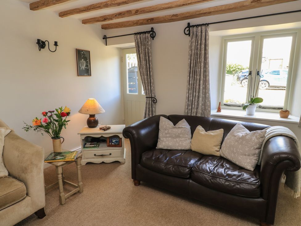 A living room with a sofa, table, lamp, and flower vase at 2 The Gardens, Lechlade