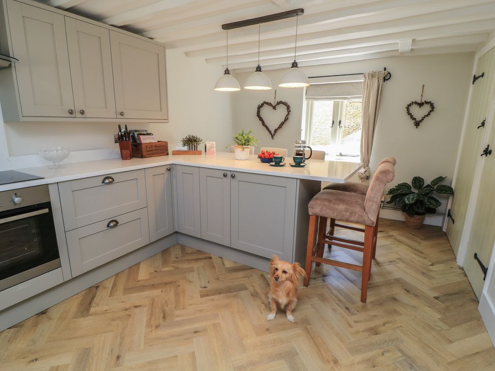 A kitchen with cabinets, a countertop, a bar stool, and a dog at 2 The Gardens Lechlade