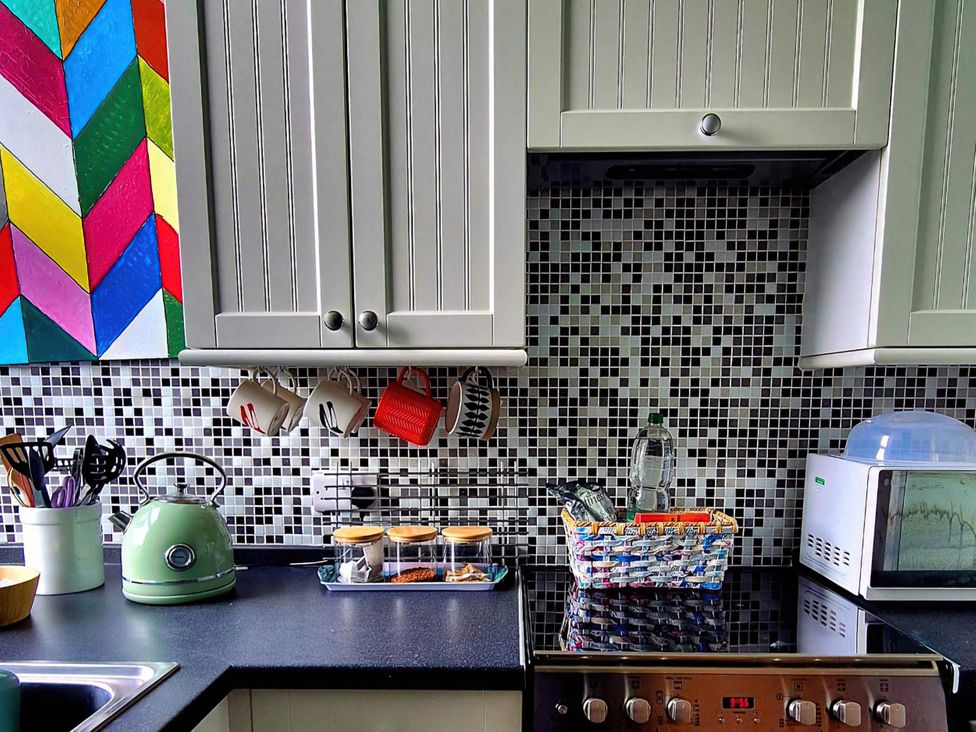 A kitchen with cabinets, mugs, kettle, spice jars, microwave, and stove at Flat 3 in Llandudno