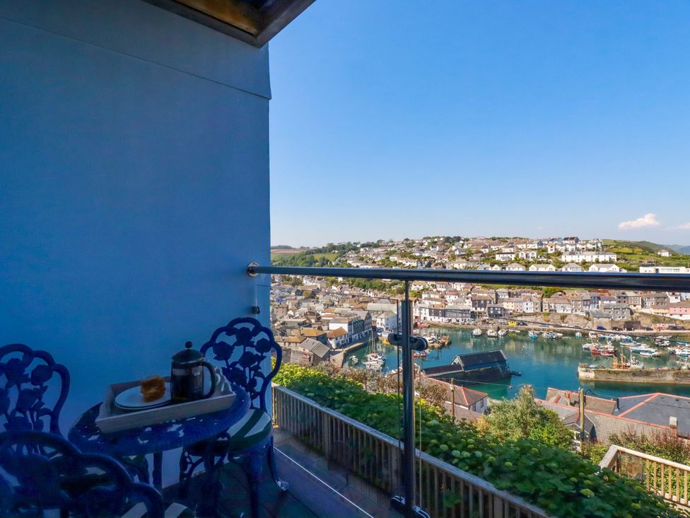 A balcony with a table and chairs overlooking a harbor at Trewollock in Mevagissey