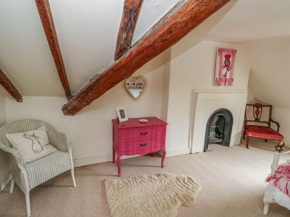 A bedroom with a pink chest of drawers and a white armchair at Sciora Cottage