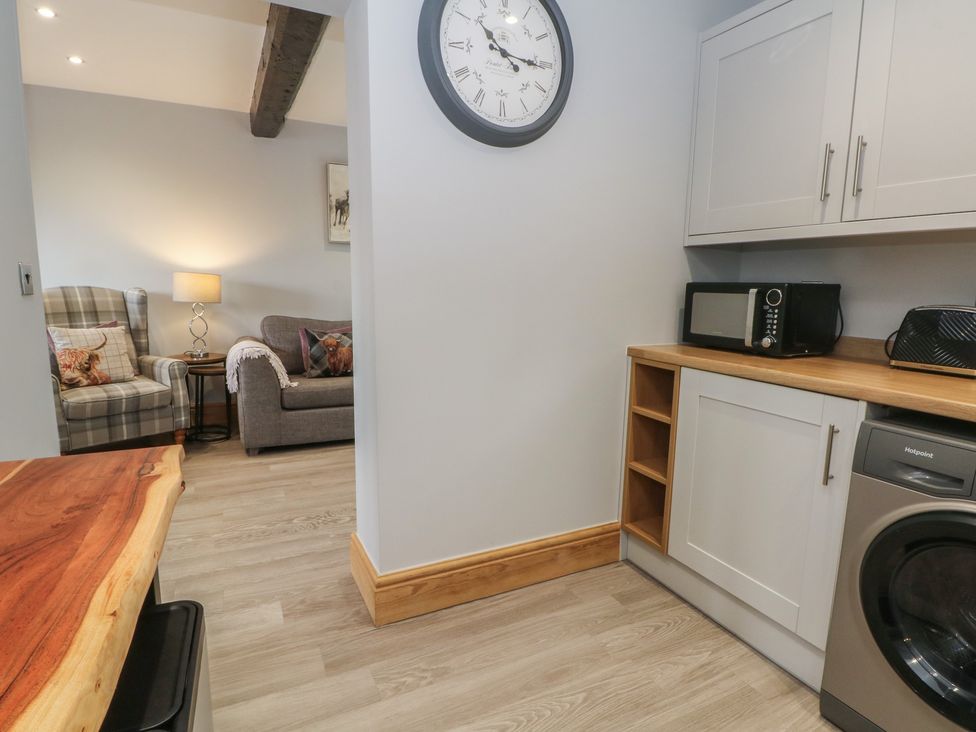 A living room with a sofa, armchair, and kitchen appliances at Barn 1 Day Green near Rode Heath