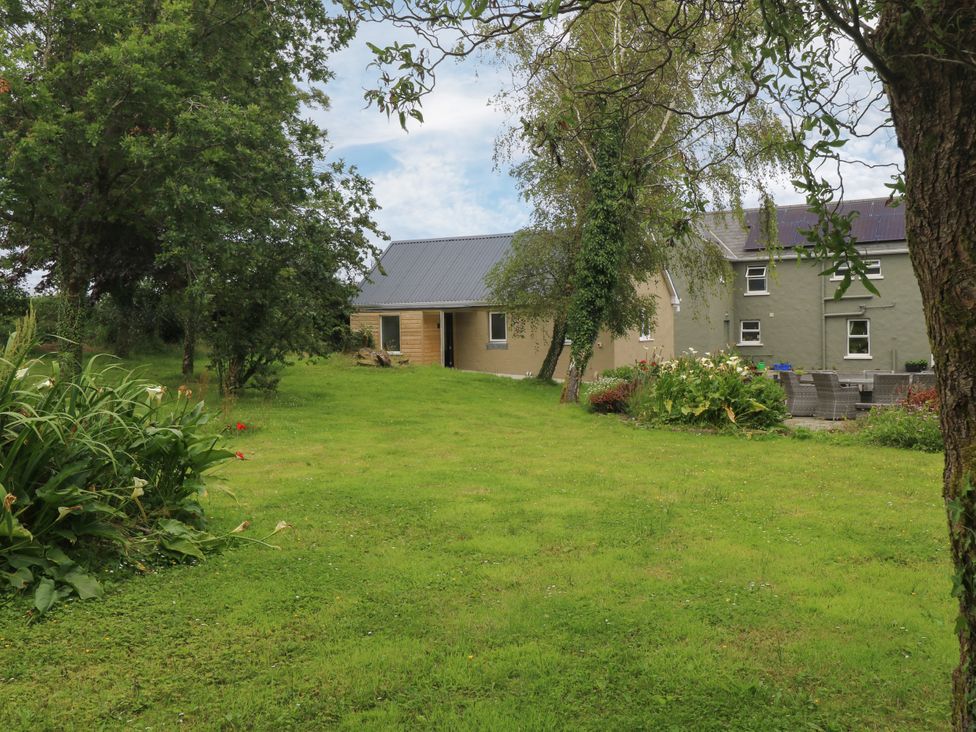 A garden with a house and trees at Mayfly Cottage
