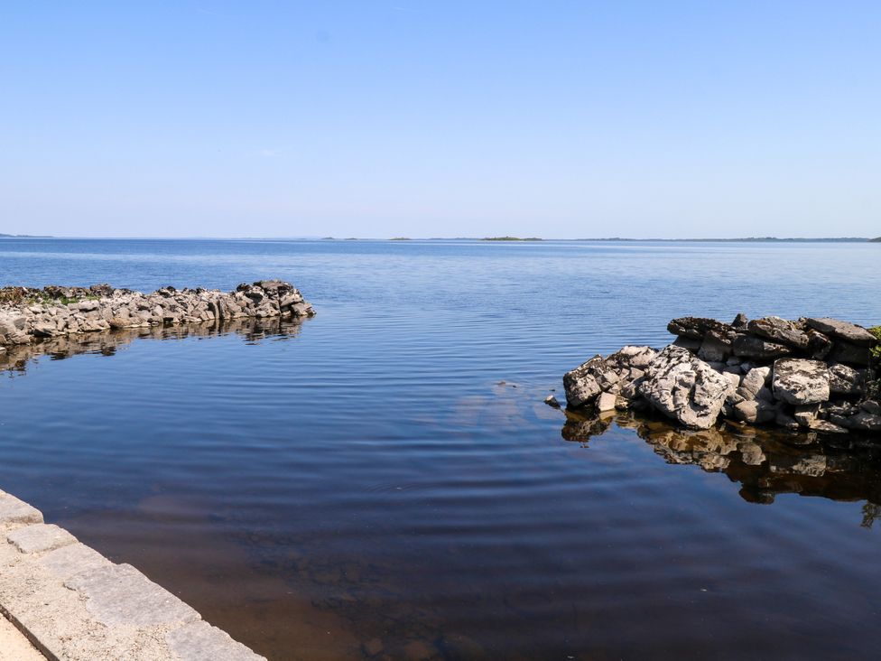 A shoreline with rocks and water under a clear sky at Mayfly Cottage