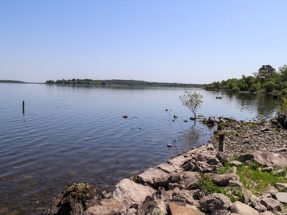A lakeside view with rocks and trees at Mayfly Cottage 